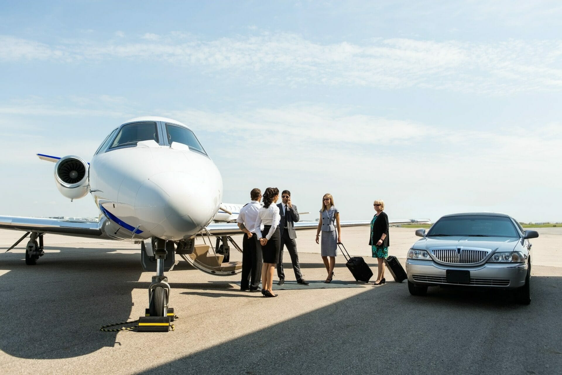 Business people with pilot and airhostess standing near private jet and limo at terminal