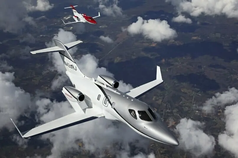 Two HondaJets Exterior aerial shot flying in formation above clouds in red and silver