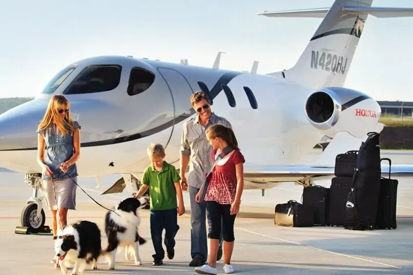 HondaJet Exterior uz zemes ar četru cilvēku ģimeni un suni, kurš iet prom no lidmašīnas "