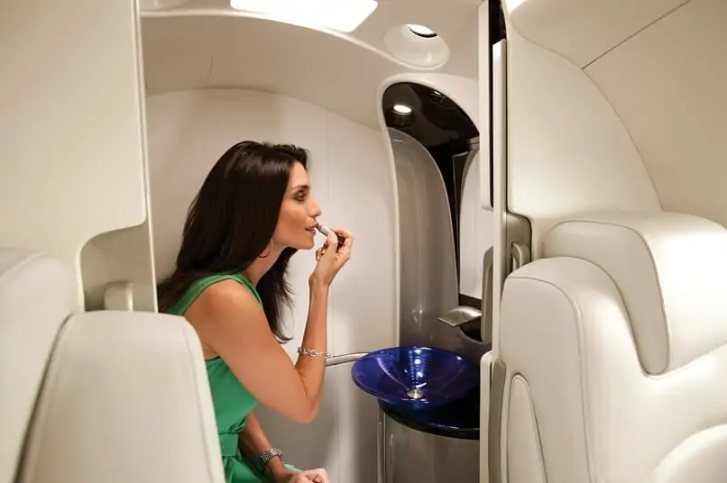 Mulher dentro de HondaJet aplicando batom no lavatório padrão do Hondajet usando o espelho de maquilhagem