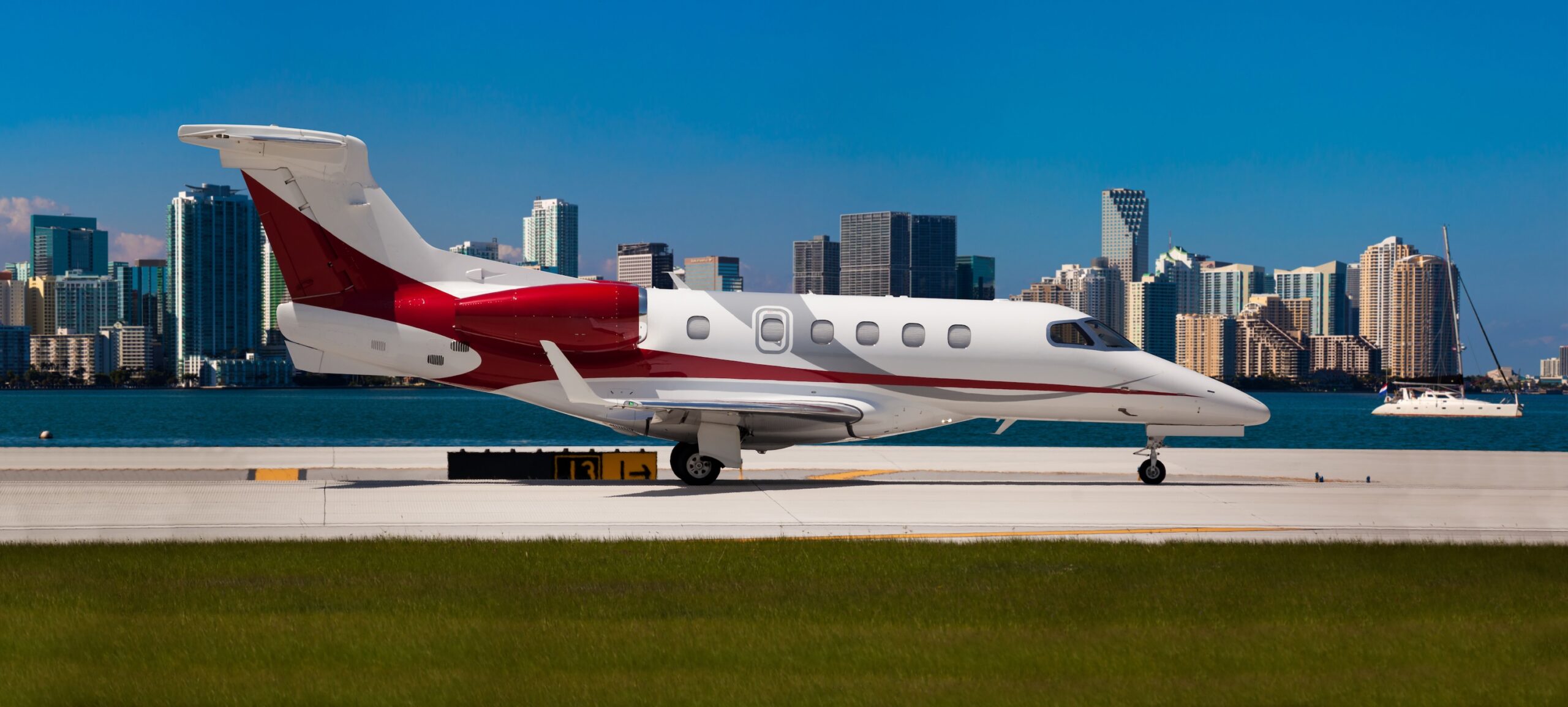 Embraer Phenom 300 jet privato con coda rossa all'aeroporto con acqua e skyline della città dietro