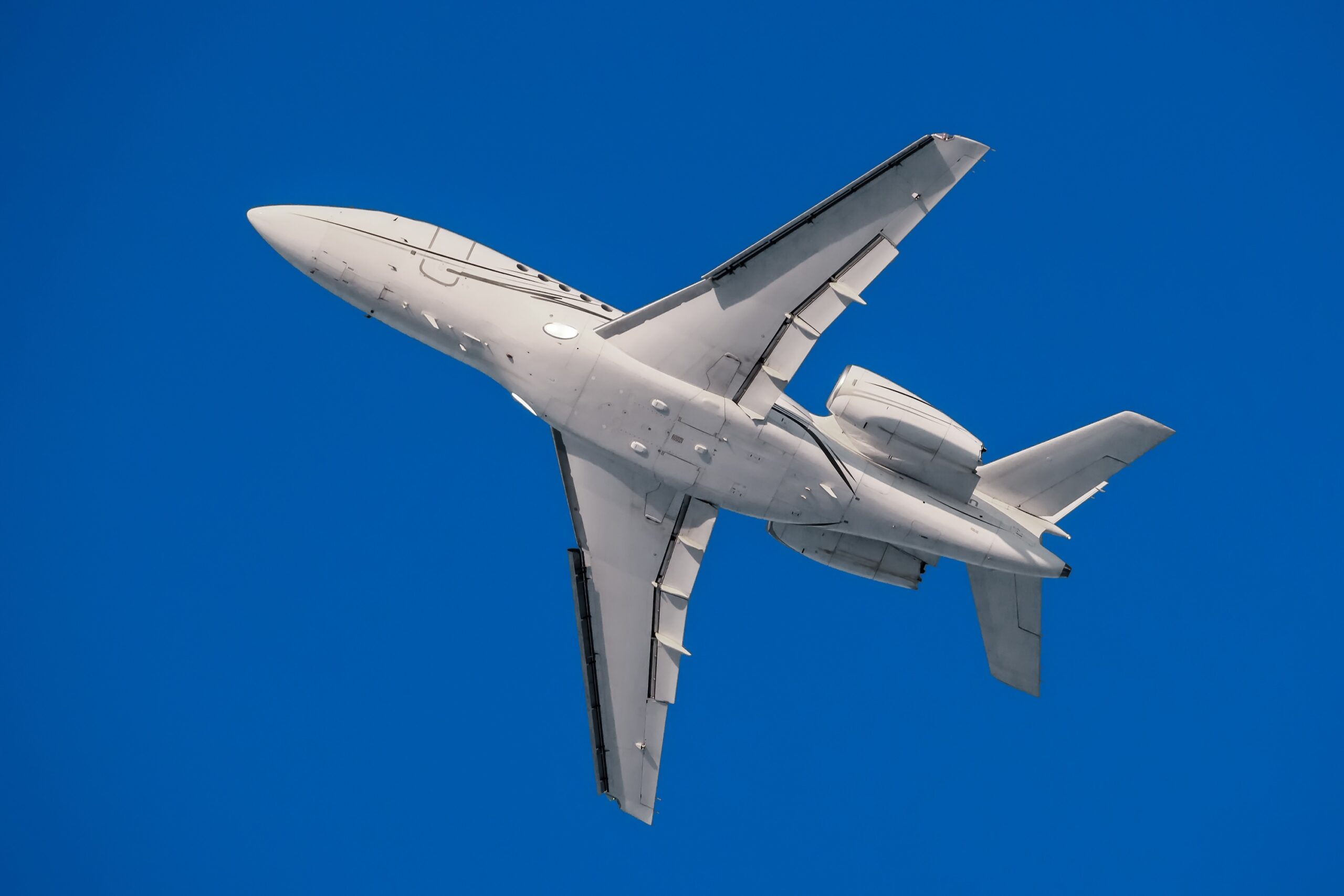 Jet privato moderno bianco nella vista inferiore del volo con cielo blu