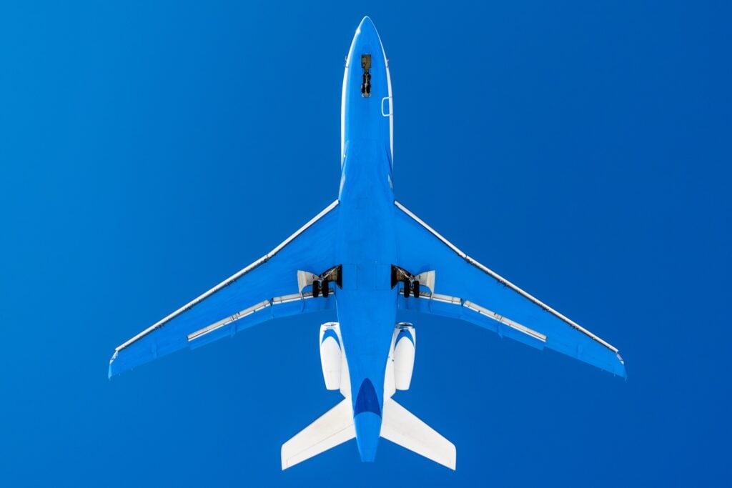 parte inferiore di un jet privato in volo con fondo blu e cielo azzurro, alto nel cielo