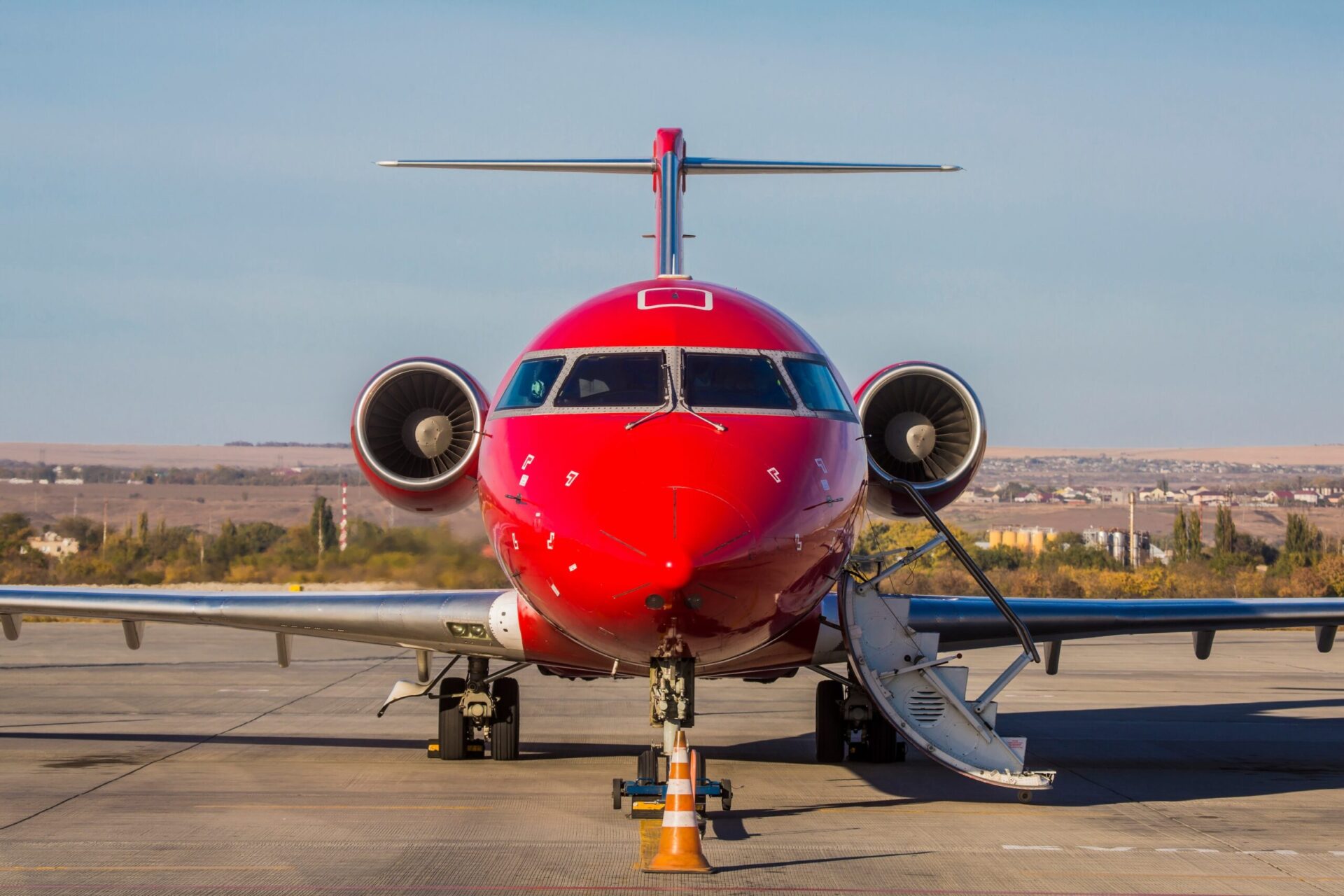 Jet privato rosso brillante parcheggiato all'aeroporto con il muso in vista e le scale estese